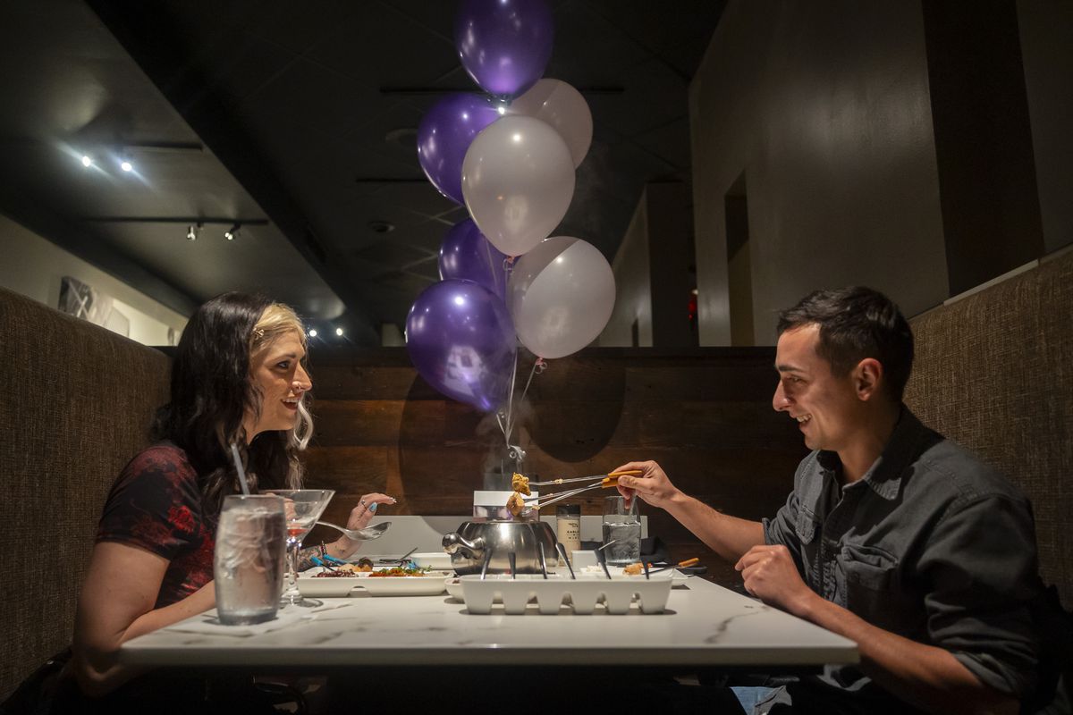Man and woman at a restaurant table with purple and silver balloons tied to the back of it and a fondue pot in the center.
