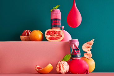Cans of Geez Louise are surrounded by peeled grapefruits, mint leaves and water balloons