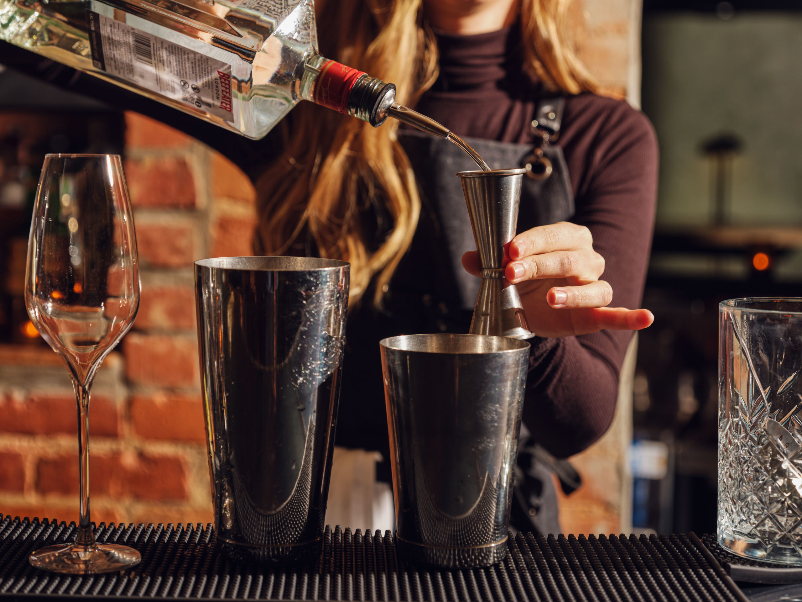 A woman behind a bar pours Beefeater gin into a cocktail jigger
