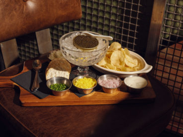 A tin of caviar on ice is served with grated egg, crème fraîche, minced shallots, kettle chips, water crackers and Tabasco