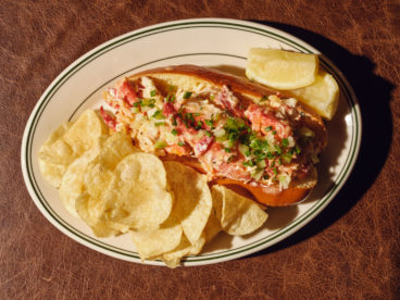 A buttered brioche bun stuffed with lobster dressed with kewpie mayo comes with a side of kettle chips and a lemon wedge