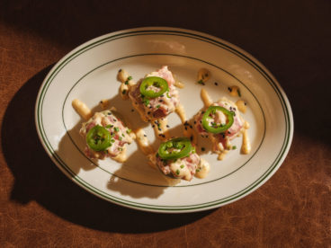 Four stacks of ahi tuna and crispy rice topped with avocado crema, lime juice, mayo, sriracha, toasted jalapeño and black sesame seeds